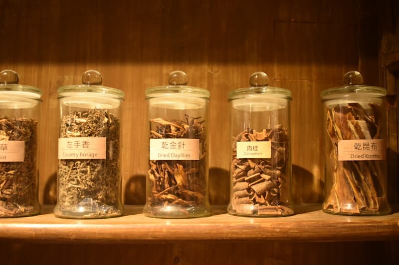 Glass jars of dried adaptogenic herbs and roots on a wooden shelf, evoking ashwagandha supplementation and nighttime use