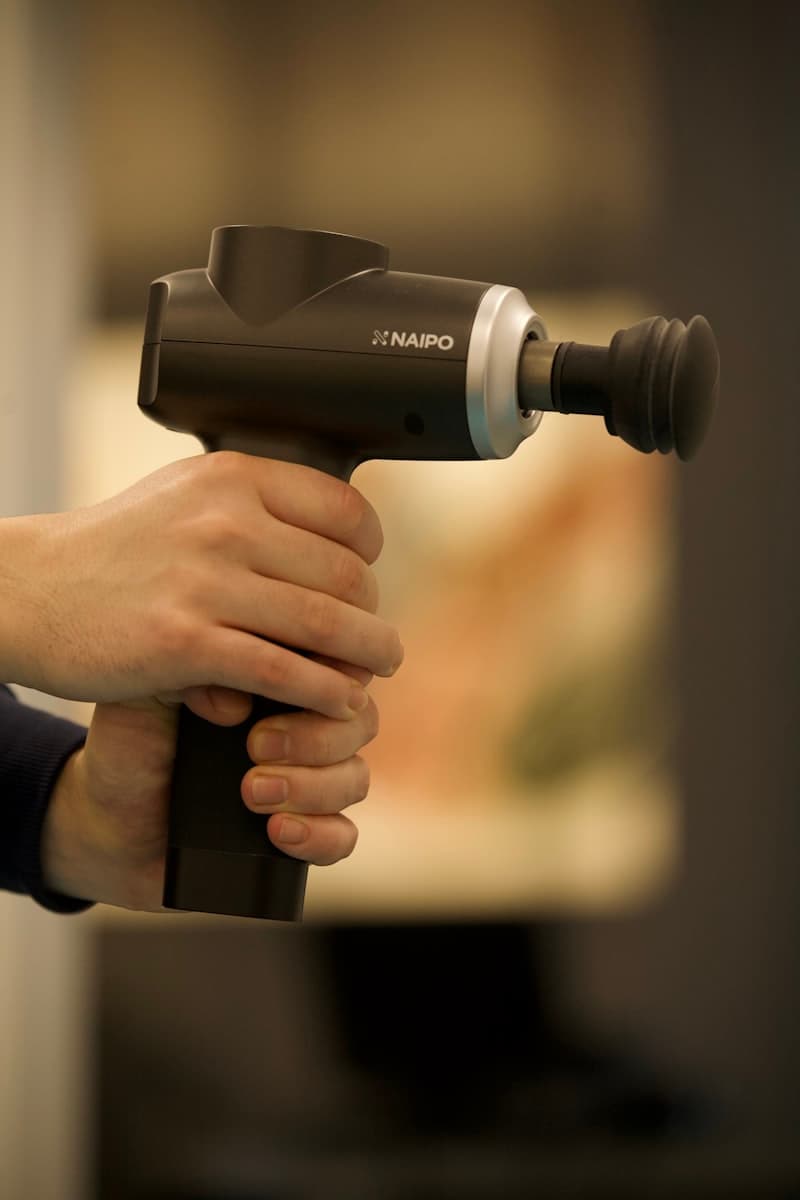 Person using a massage gun on their shoulder — percussion therapy mechanism in action